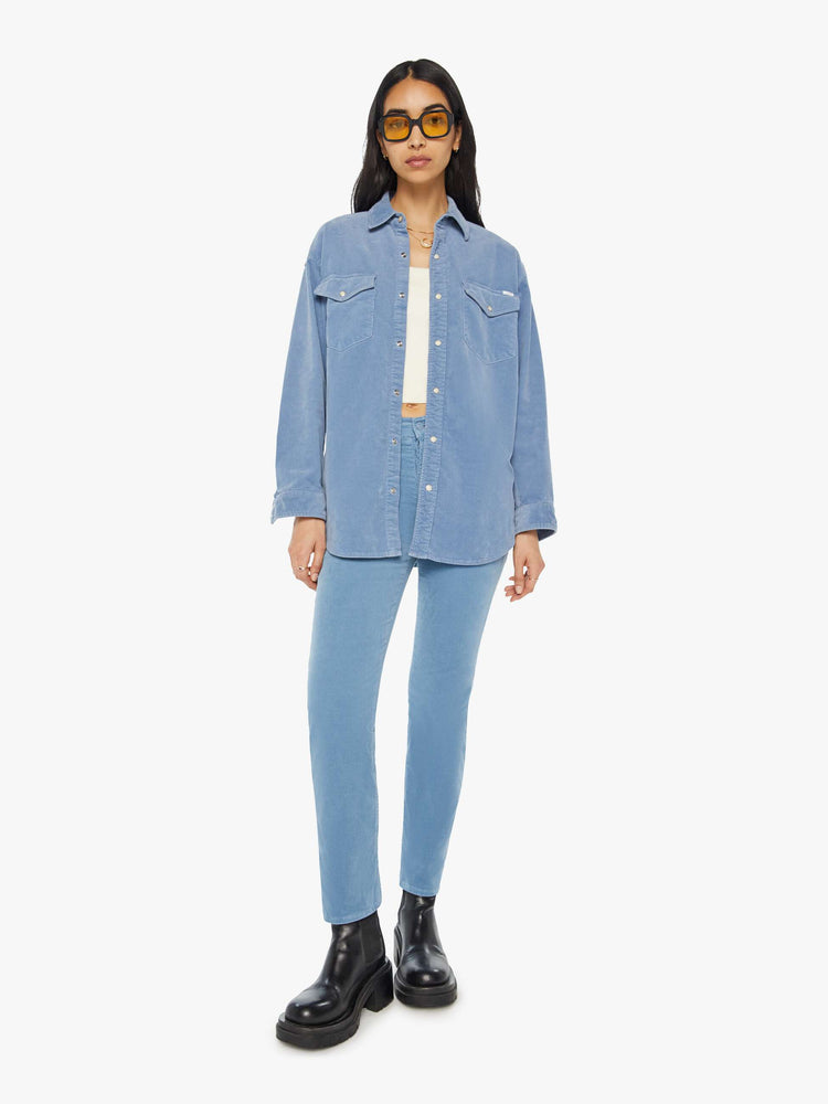 Full body view of a woman light blue corduroy western-inspired button-up with drop shoulders, patch pockets, snap closures and a curved hem.