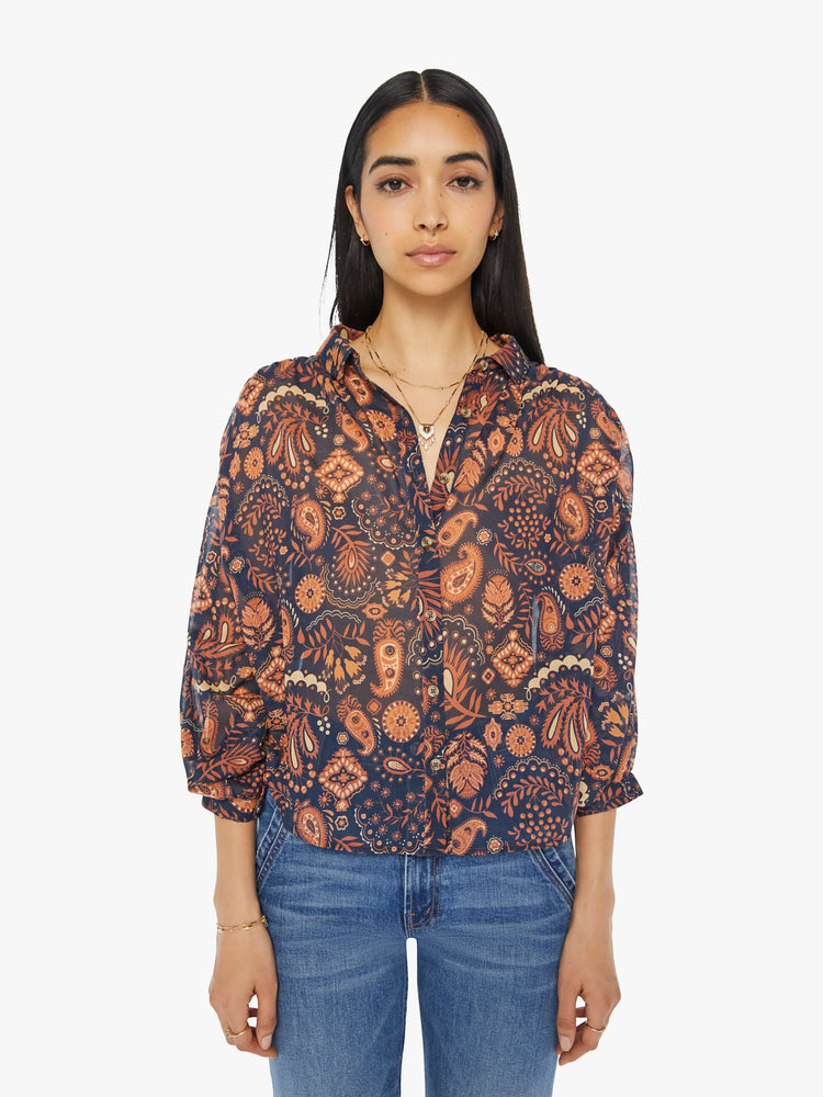 Front view of a woman navy and orange paisley print button down blouse with a collared V-neck, 3/4 length balloon sleeves and curved hem.