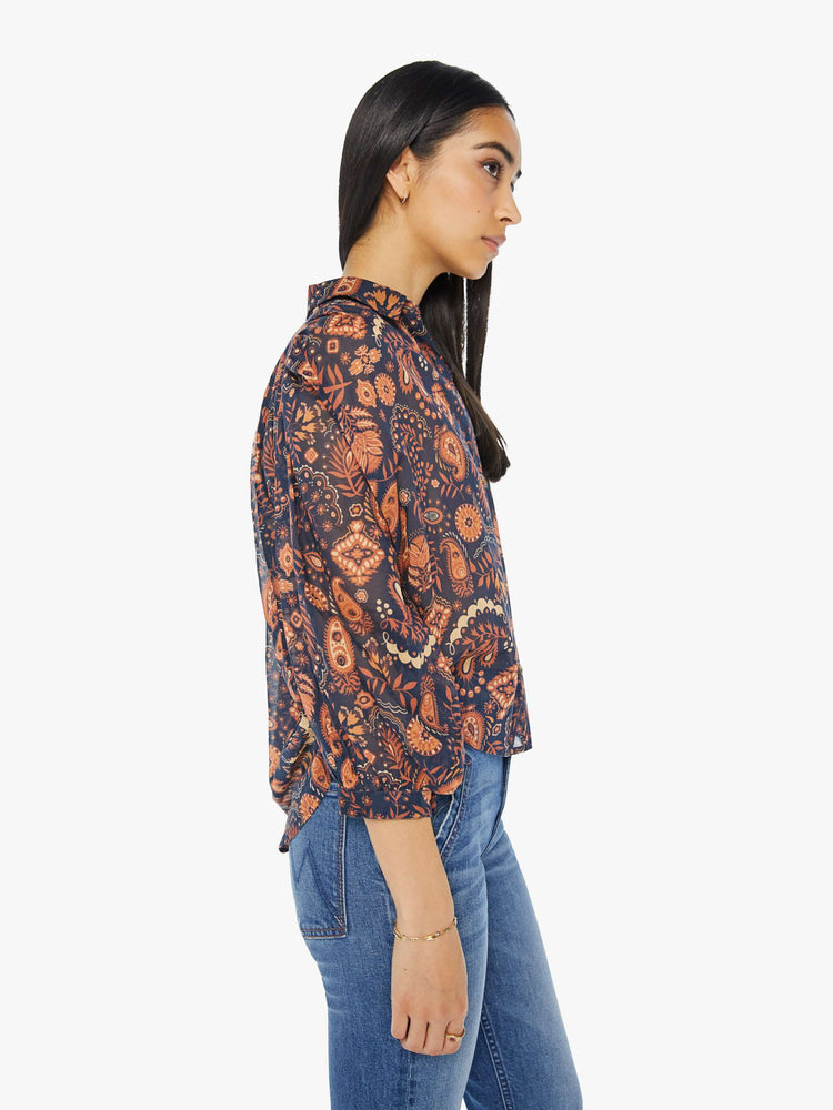 Side view of a woman navy and orange paisley print button down blouse with a collared V-neck, 3/4 length balloon sleeves and curved hem.