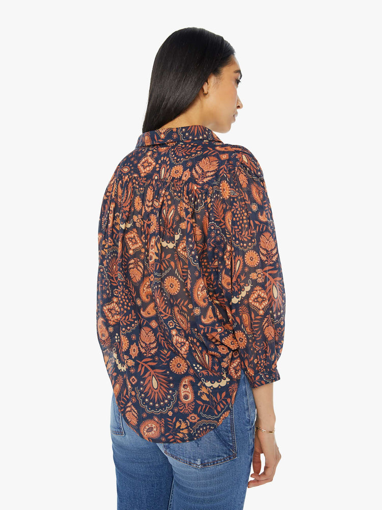 Back view of a woman navy and orange paisley print button down blouse with a collared V-neck, 3/4 length balloon sleeves and curved hem.