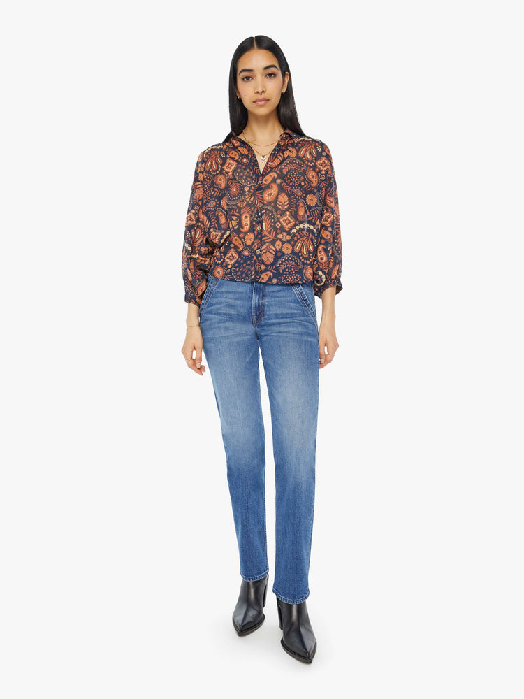 Full body view of a woman navy and orange paisley print button down blouse with a collared V-neck, 3/4 length balloon sleeves and curved hem.