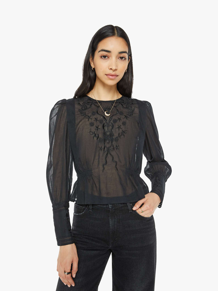 Front view of a woman in black blouse with long puff sleeves, a gathered elastic waist, long hems at the wrists that button and a cropped fit.