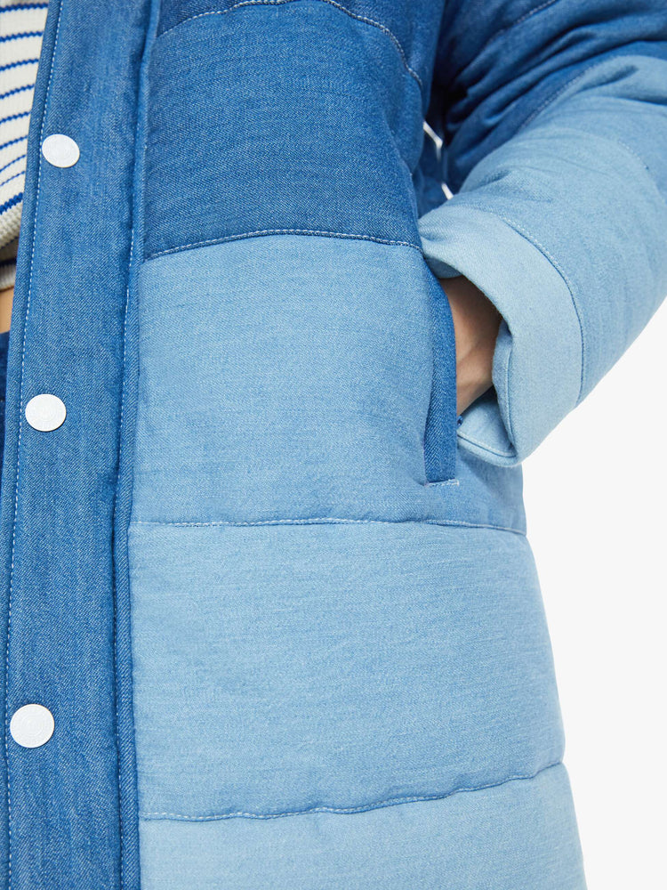 Swatch view of a woman in a knee length puffer jacket with a stacked collar side slit pockets and button down the front in shades of blue.