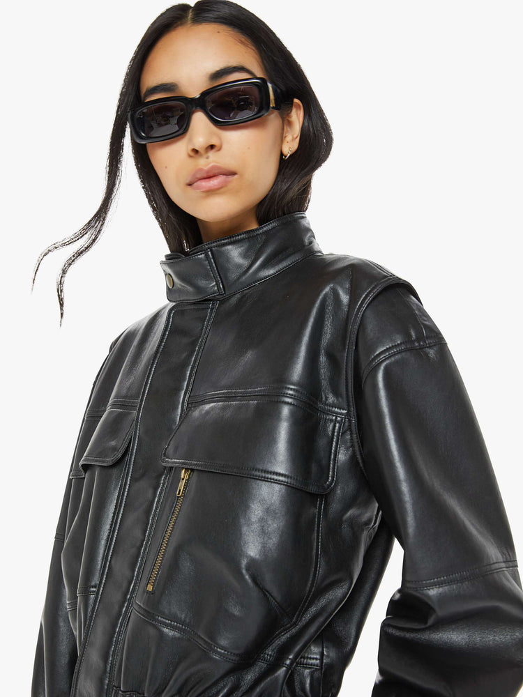 Close up view of a woman in a leather black parka  with a stacked collar, patch pockets, elastic at the waist and wrists, a zip closure and drawstring hem that hits mid-thigh. 