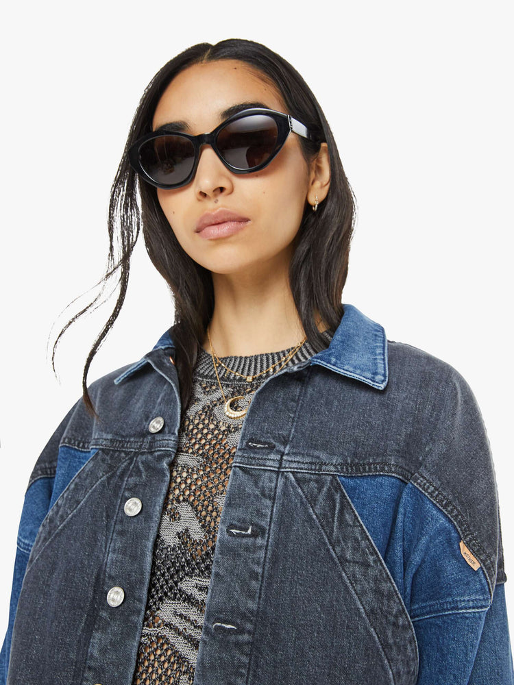 Close up front  view of a woman in med blue wash with black  denim jacket with drop shoulders, angled patch pockets on the chest and a classic fit. 