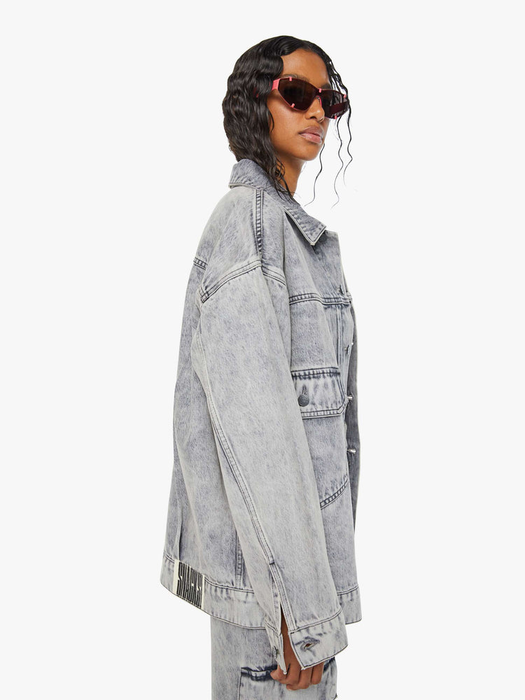 Side view of a woman in acid-washed grey oversized denim jacket features large patch pockets, drop shoulders and a boxy fit. 