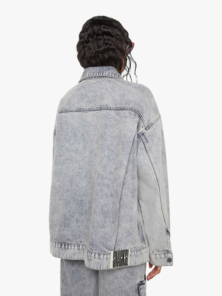 Back view of a woman in acid-washed grey oversized denim jacket features large patch pockets, drop shoulders and a boxy fit. 