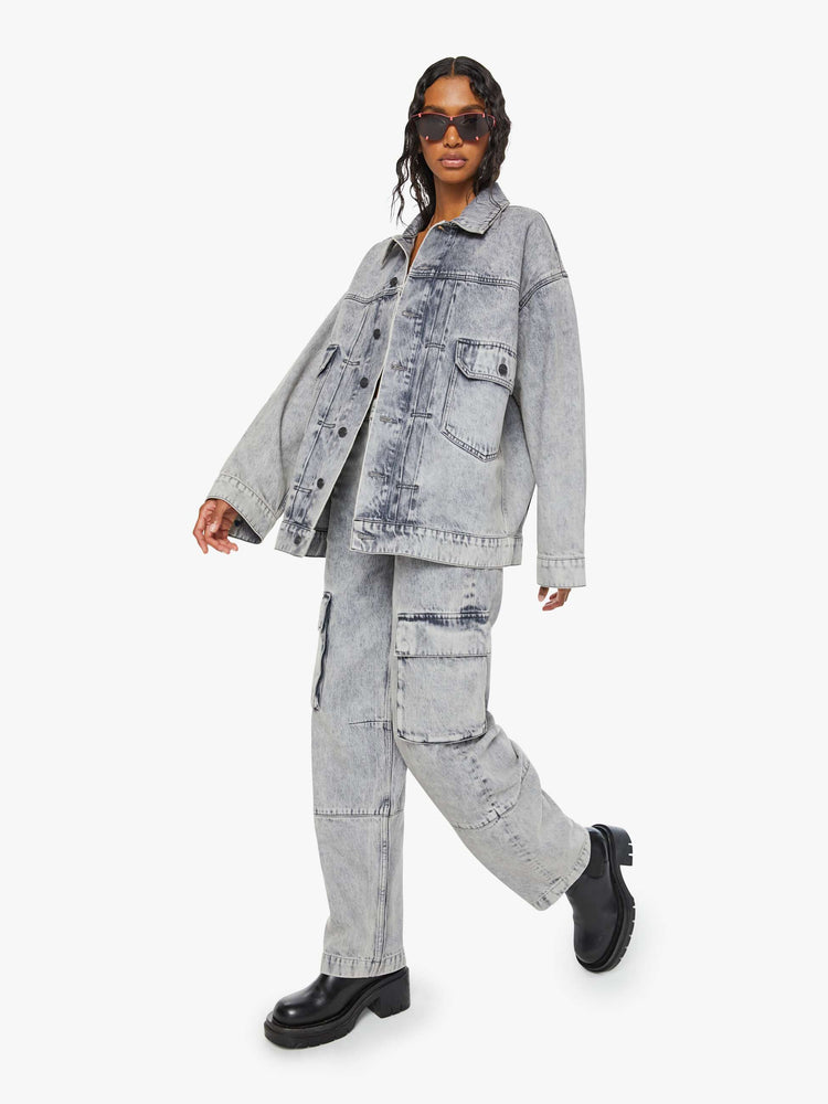 Full angled view of a woman in acid-washed grey oversized denim jacket features large patch pockets, drop shoulders and a boxy fit. 