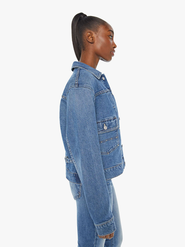 Side view of a woman denim jacket designed with drop shoulders, low patch pockets, adjustable tabs at the waist and pleated details down the front.