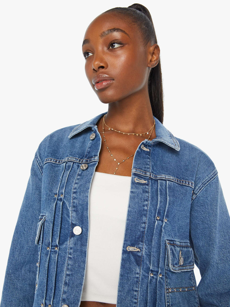 Close up view of a woman denim jacket designed with drop shoulders, low patch pockets, adjustable tabs at the waist and pleated details down the front.