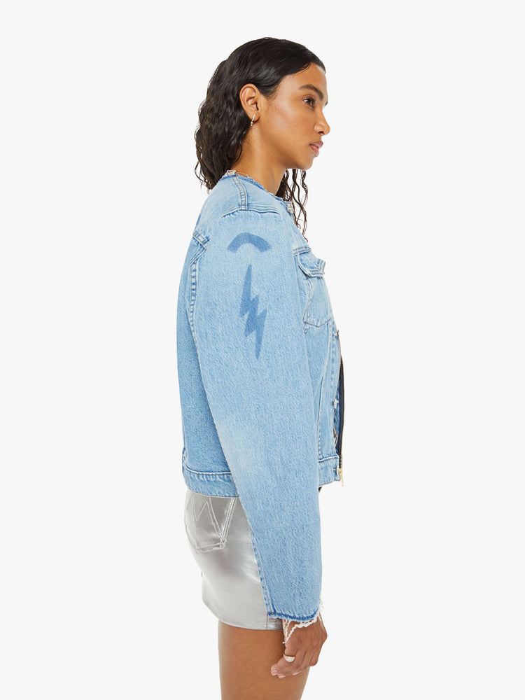 Side view of a woman in deconstructed denim jacket with  a raw crewneck, patch pockets, buttons down the front and a zip closure in a light blue wash with shadowy of old patches.