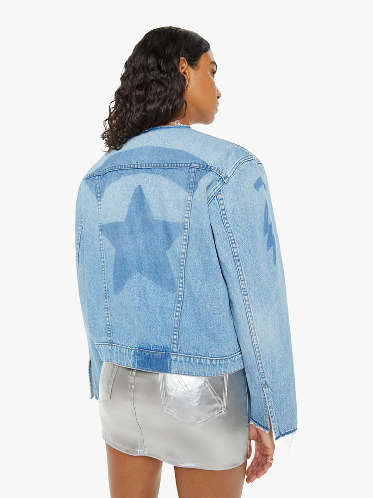 Back view of a woman in deconstructed denim jacket with  a raw crewneck, patch pockets, buttons down the front and a zip closure in a light blue wash with shadowy of old patches.