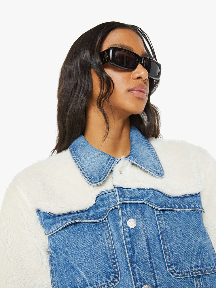 Close up view of a mid blue classic denim jacket with faux sherpa with patch pockets and a boxy, slightly cropped fit.