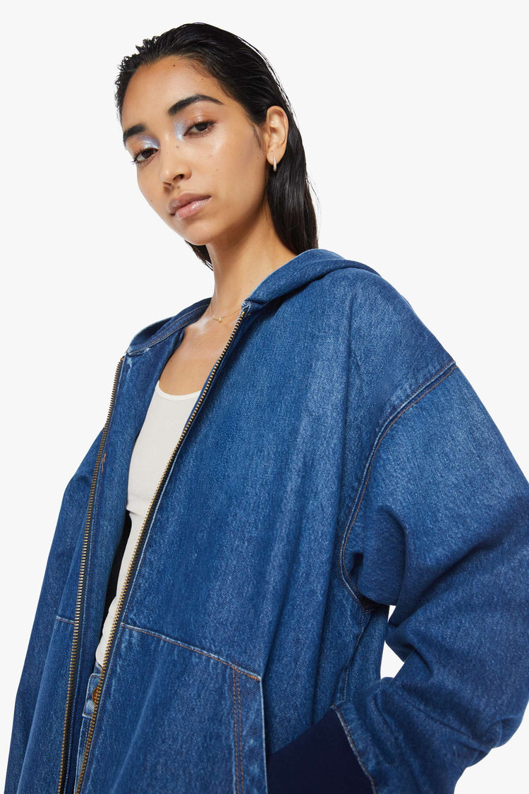 Close up view of a woman in mid blue denim jacket with drop shoulders, oversized patch pockets, ribbed hems and a loose fit. 