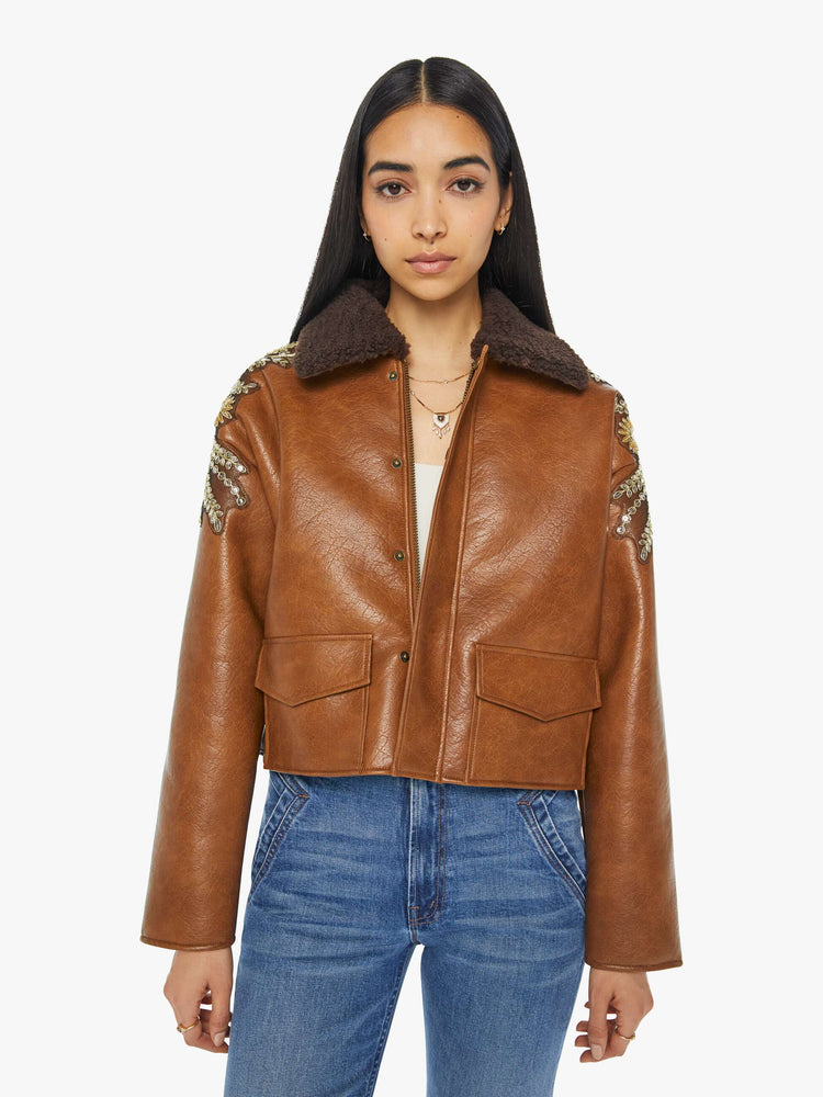 Front view of a woman in collard jacket with a zip closure that snaps, front patch pockets, oversized shoulders, drop sleeves and a cropped hem in a brown faux leather.