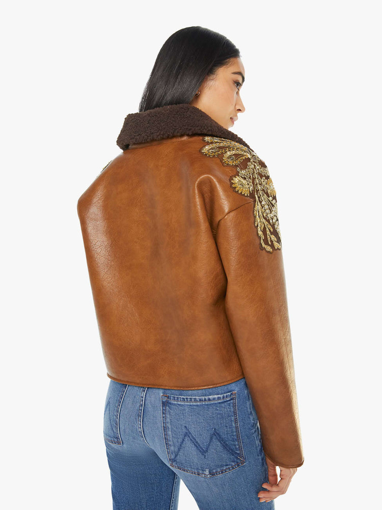 Back view of a woman in collard jacket with a zip closure that snaps, front patch pockets, oversized shoulders, drop sleeves and a cropped hem in a brown faux leather.