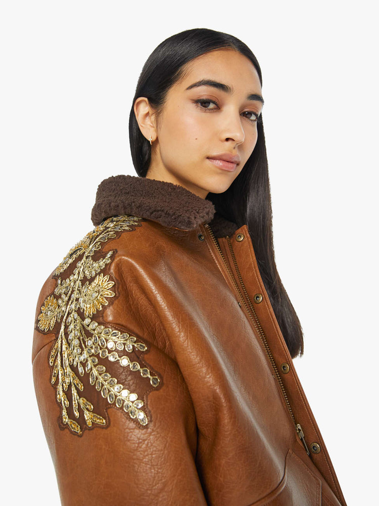 Close up view of a woman in collard jacket with a zip closure that snaps, front patch pockets, oversized shoulders, drop sleeves and a cropped hem in a brown faux leather.