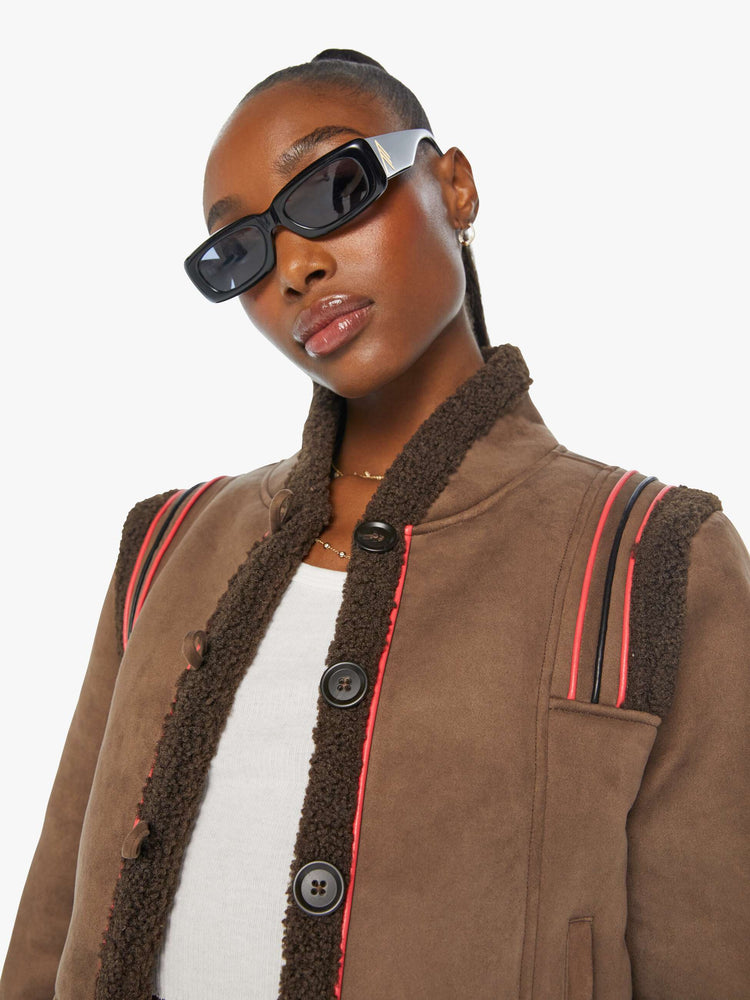 Close up view of a woman in a brown faux button-up jacket with red details and faux-shearling trim.