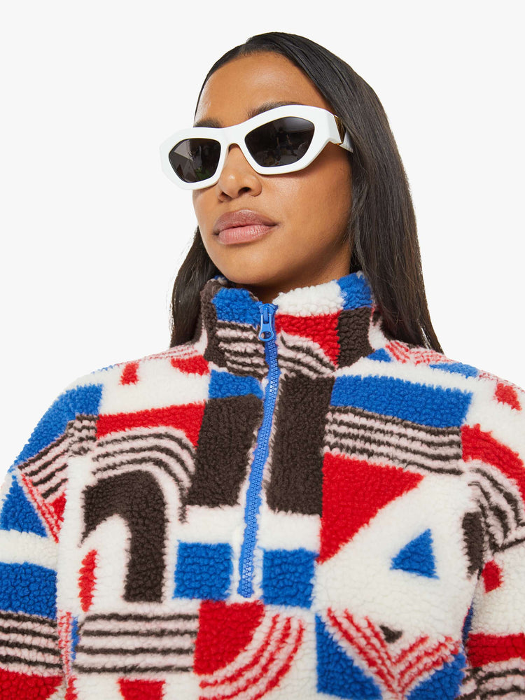 Close up view of a woman in a quarter-zip jacket with a stacked collar, drop shoulders, zip pockets and a loose, boxy fit in red, white, blue and brown graphic print.