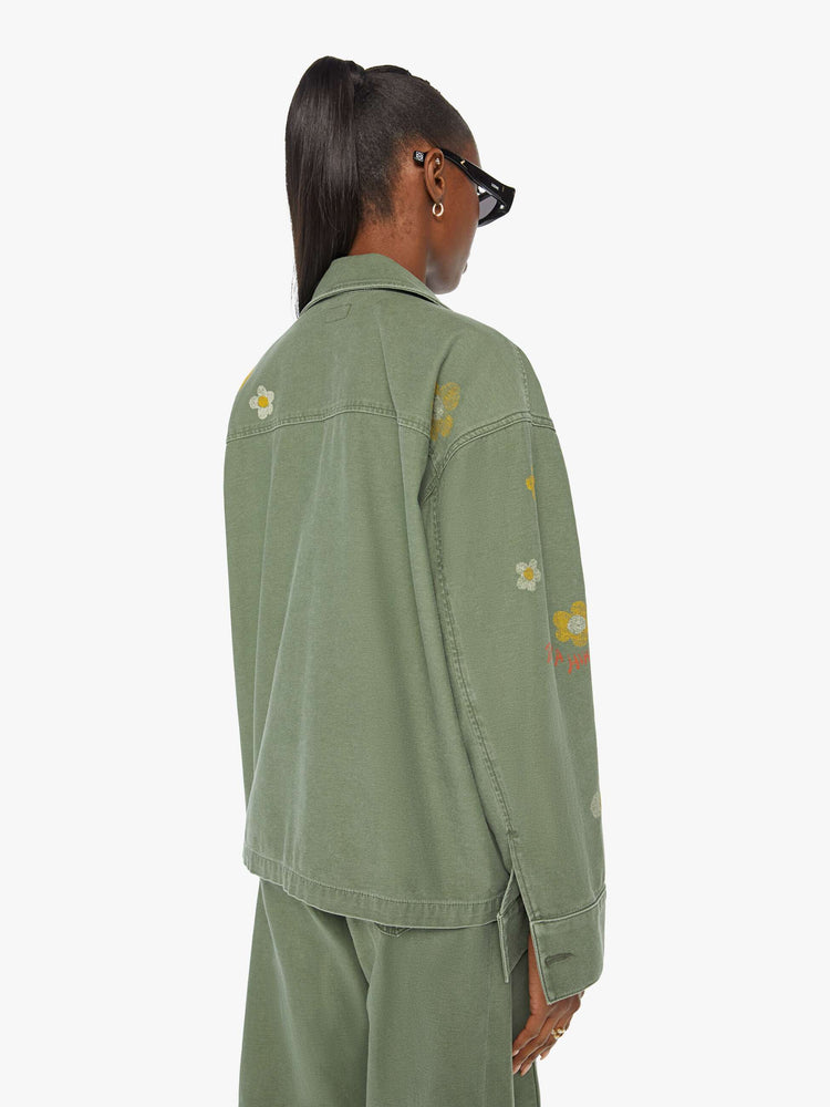 Back view of a woman in a military green flower and rainbow embroidered collared jacket with oversized patch pockets, a zip closure that snaps shut.