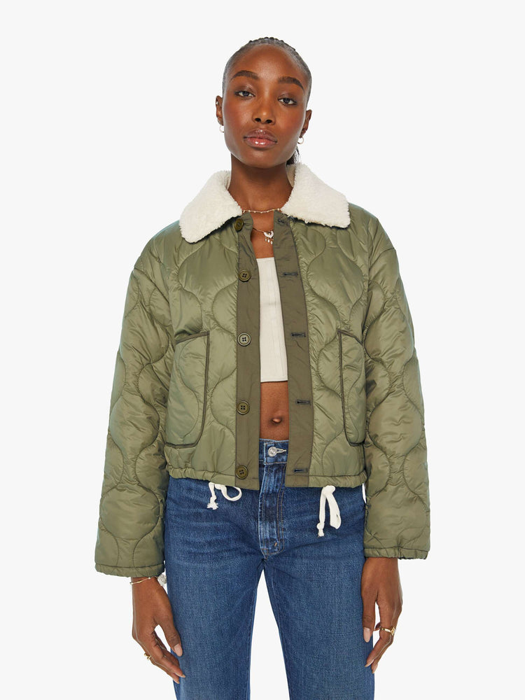 Front view of a woman in a quilted green military liner jacket features drop shoulders, patch pockets, buttons down the front and a cropped, boxy fit.