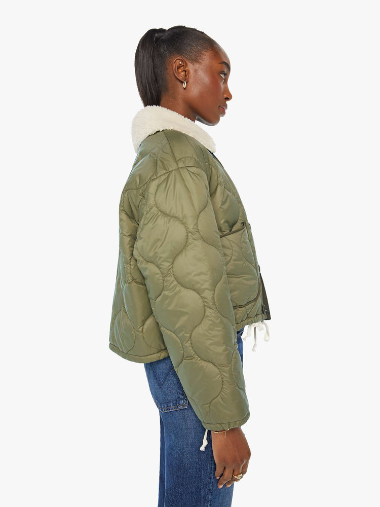 Side view of a woman in a quilted green military liner jacket features drop shoulders, patch pockets, buttons down the front and a cropped, boxy fit.