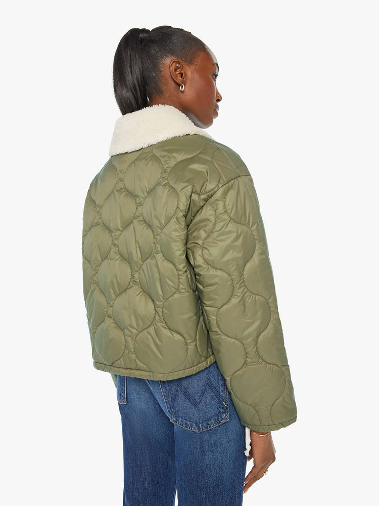 Back view of a woman in a quilted green military liner jacket features drop shoulders, patch pockets, buttons down the front and a cropped, boxy fit.