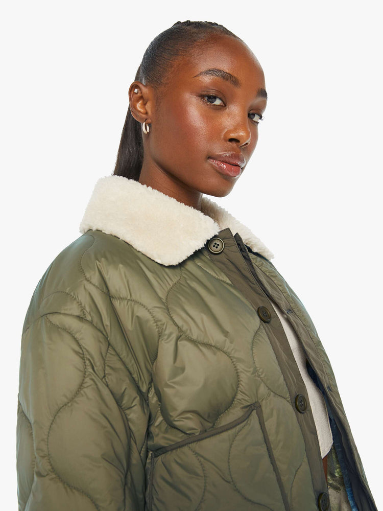 Detailed view of a woman in a quilted green military liner jacket features drop shoulders, patch pockets, buttons down the front and a cropped, boxy fit.