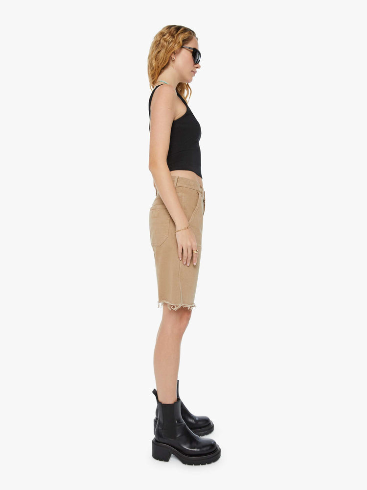 Side view of a woman in dark khaki high-waisted bermuda shorts designed to sit lower on the hips with a long 9.5-inch inseam and a frayed hem.