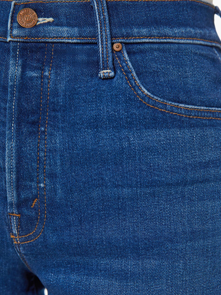 Detailed view of a woman in dark blue high-waisted jean shorts with a button fly and a frayed hem. 