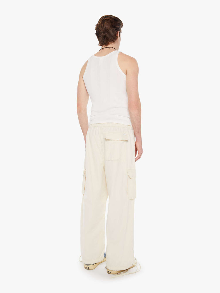 Back view of a men in a creamy white drawstring cargo pants with a loose wide-leg, patch pockets, a 26.5-inch inseam and ties at the hems.