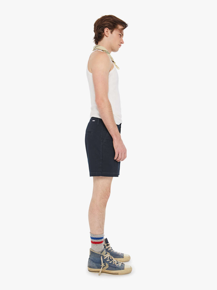 Side view of a man in a navy blue shorts with a mid rise, slit pockets and a 6-inch inseam with a clean hem.