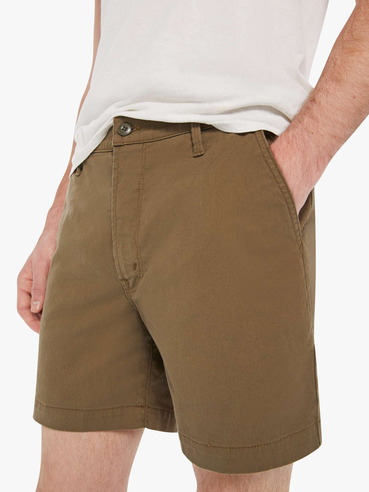 Close up view of a man in a military green short with a mid-rise, slit pockets and a 6-inch inseam with a clean hem.