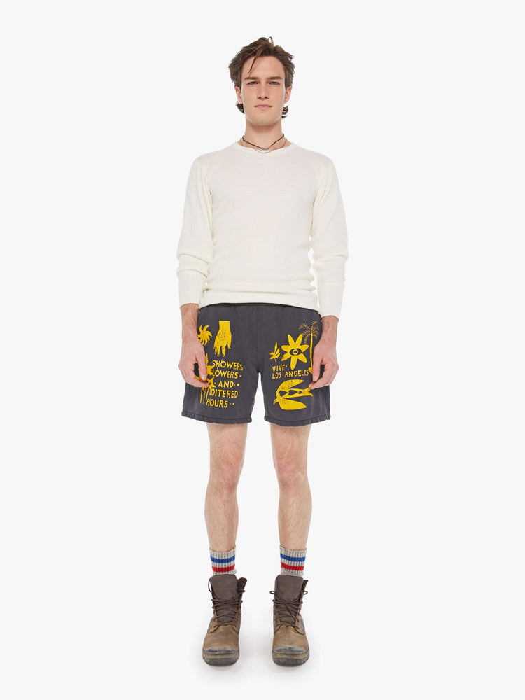 Front view of a man's faded black with yellow graphic sweatshorts with a loose wide leg, 7.5-inch inseam and a raw hem.