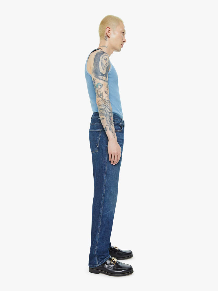 Side view of a man in a straight-leg jean with a mid rise, ankle-length inseam and a clean hem in a dark blue wash.