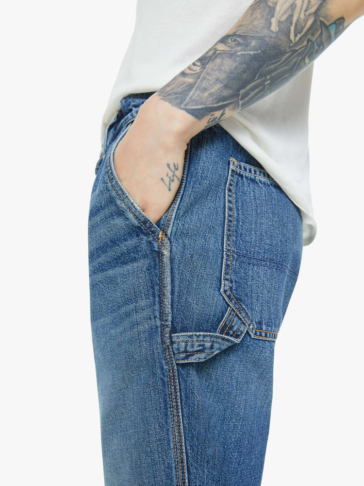 Close up view of a man in mid-blue wash classic pant with utilitarian pockets, a hammer loop and relaxed leg.