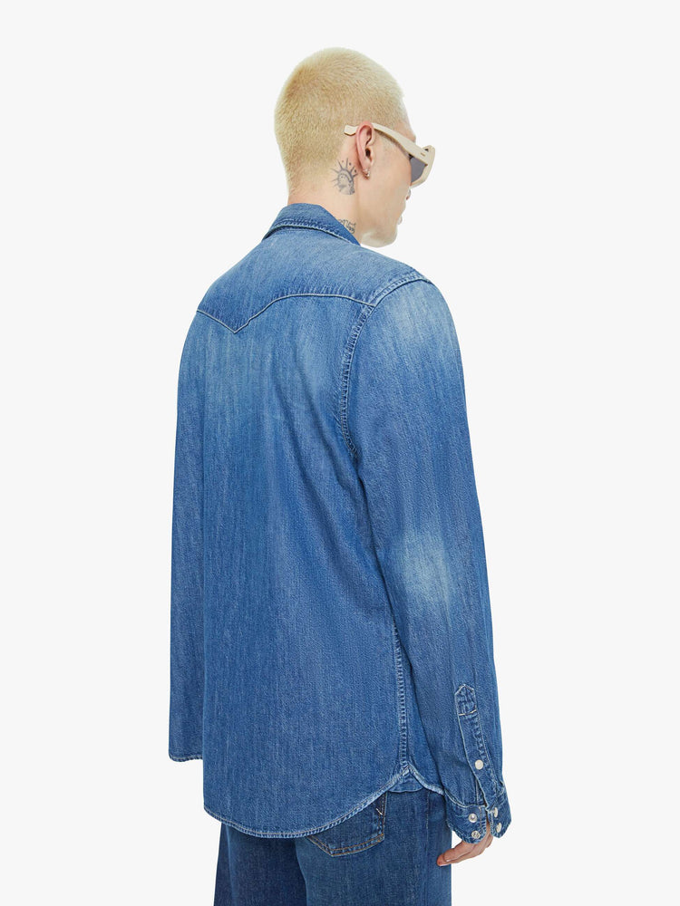 Back view of a man in a mid-blue classic button down with flap patch pockets, long sleeves and a curved hem.