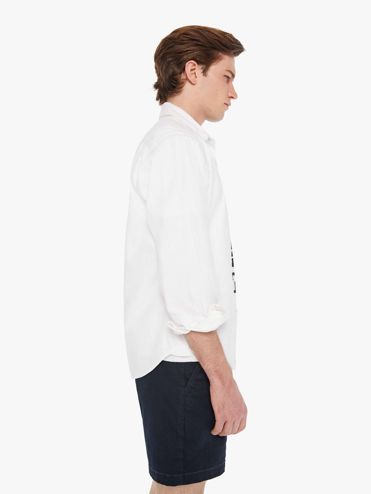 Side view a man in a white collared button-up with a patch pocket and a slightly curved hem.