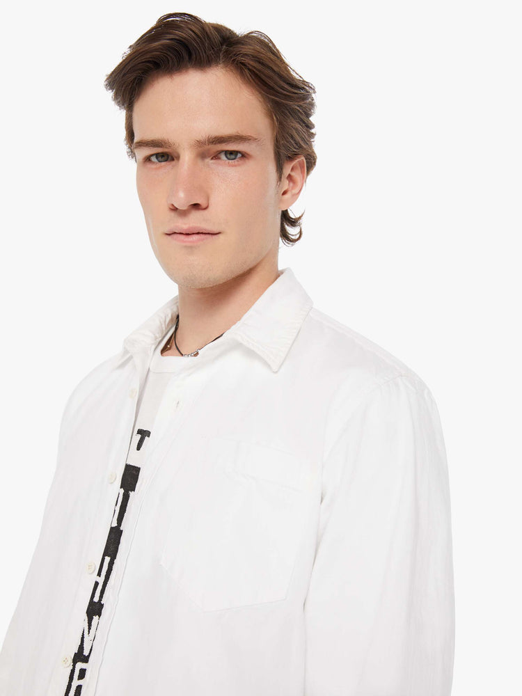 Close up view a man in a white collared button-up with a patch pocket and a slightly curved hem.