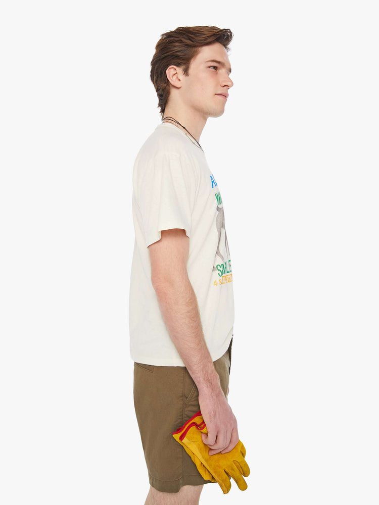 Side view of a man in a cream oversized tee with drop shoulders and a loose fit that features a faded dog graphic with colorful text on the front.