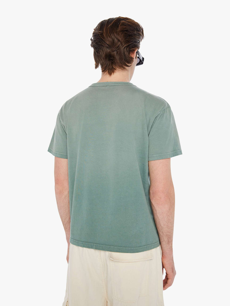 Back view of a man in a pale green oversized tee with drop shoulders and a loose fit featuring an off-white faded text graphic.