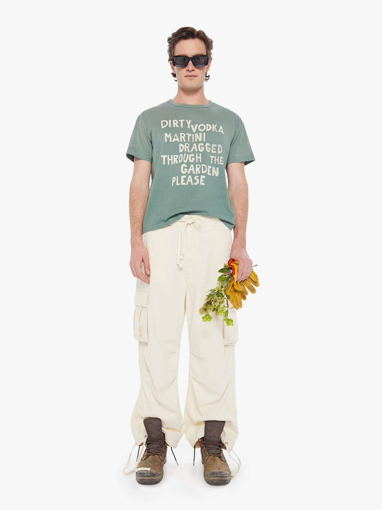 Full front view of a man in a pale green oversized tee with drop shoulders and a loose fit featuring an off-white faded text graphic.