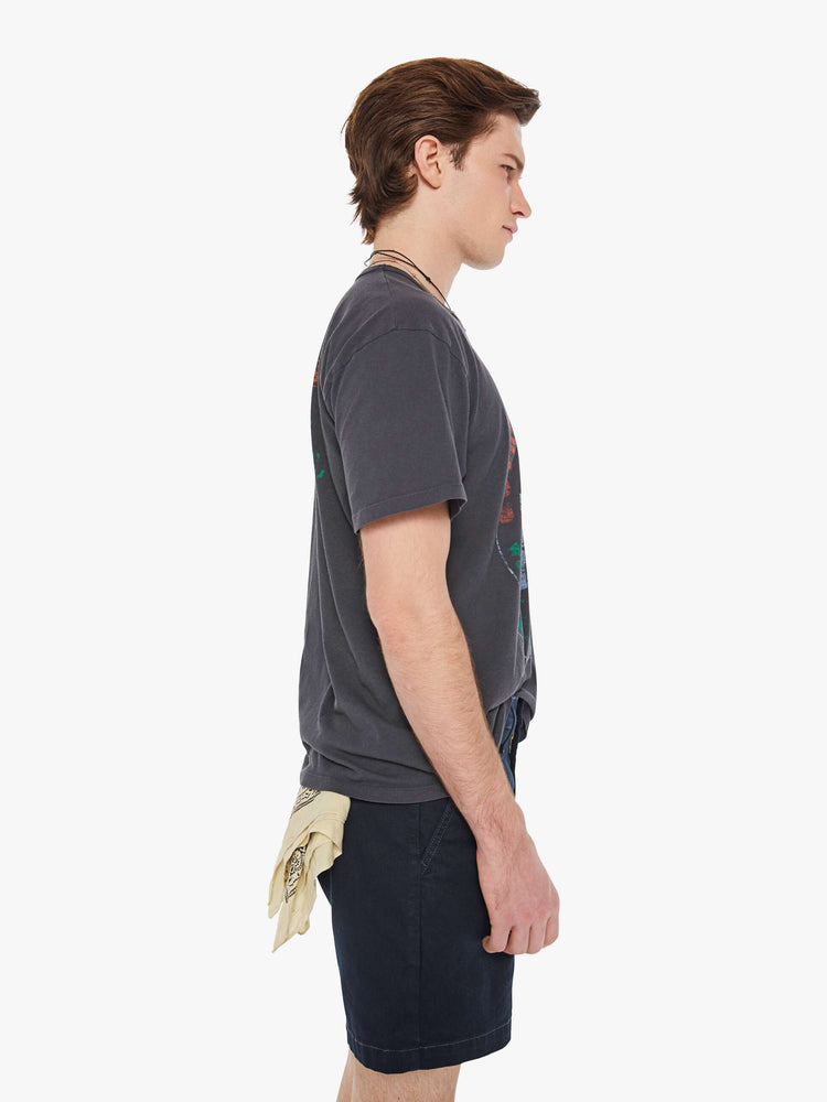 Side view of a man in a faded black oversized tee with drop shoulders and a loose fit featuring a vintage inspired faded graphic.