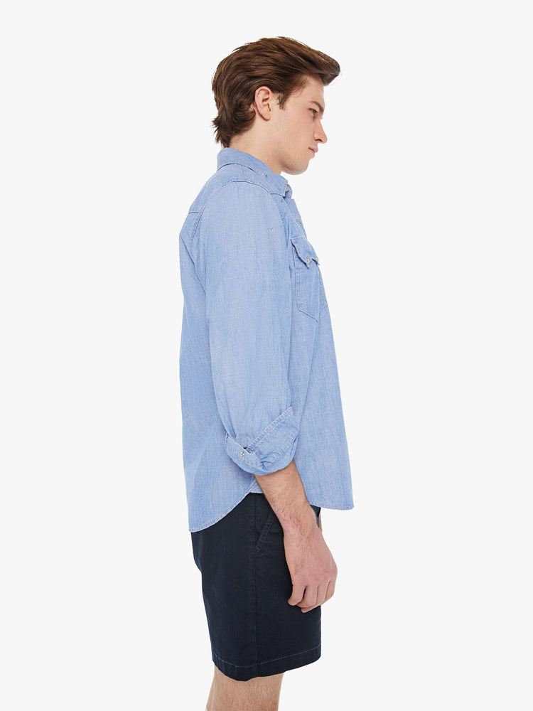 Side view of a man in a light blue cotton button-up with a Western-inspired yolk, scalloped flap patch pockets, long sleeves and a curved hem.