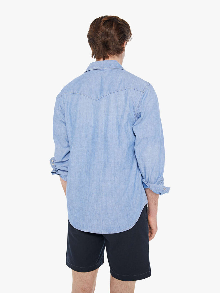 Back view of a man in a light blue cotton button-up with a Western-inspired yolk, scalloped flap patch pockets, long sleeves and a curved hem.