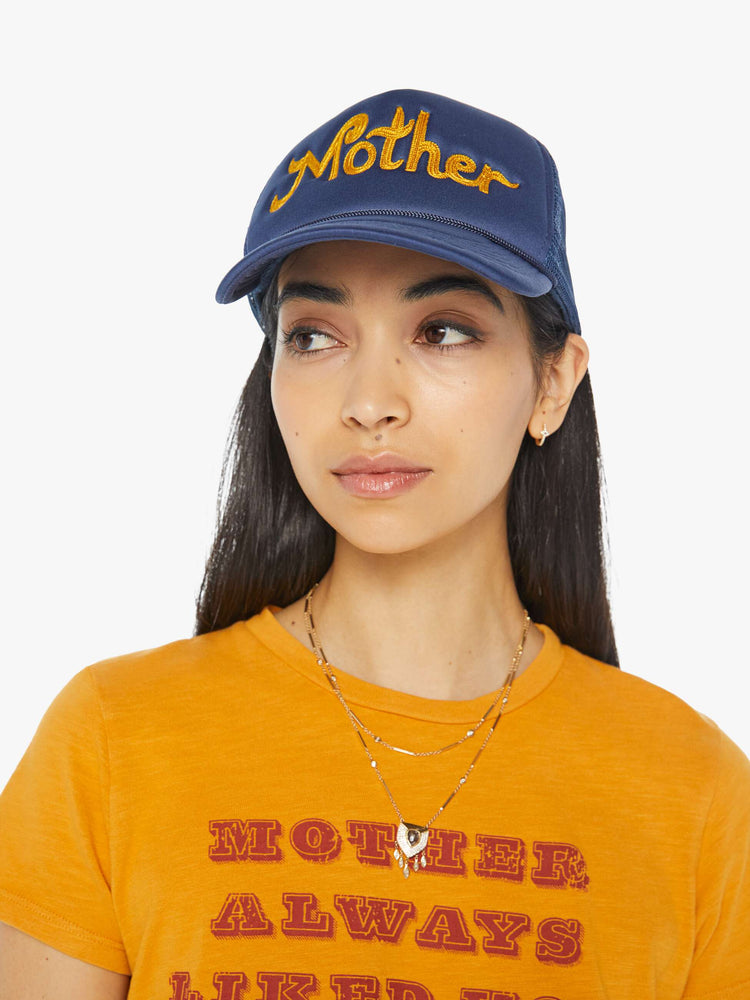 Front on model view of a vintage-inspired trucker hat designed in navy with MOTHER's name in golden yellow on the front.