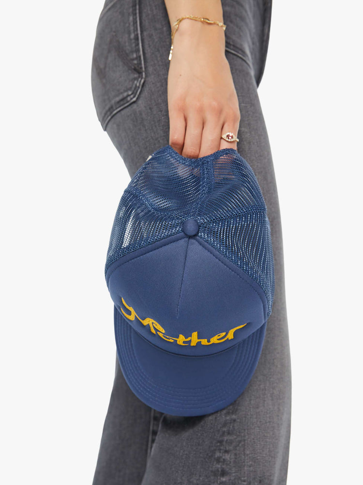 hand down on model view of a vintage-inspired trucker hat designed in navy with MOTHER's name in golden yellow on the front.