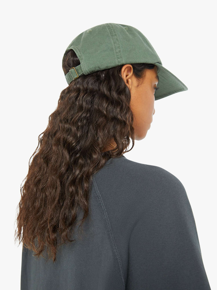 Detailed back view of a woman in a faded sage green vintage-inspired baseball hat with a golden-yellow sunset graphic and MOTHER's name embroidered on the front.