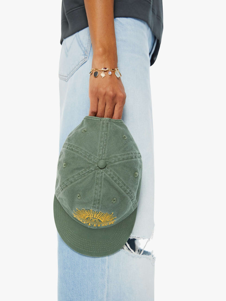 Detailed top view of a woman in a faded sage green vintage-inspired baseball hat with a golden-yellow sunset graphic and MOTHER's name embroidered on the front.