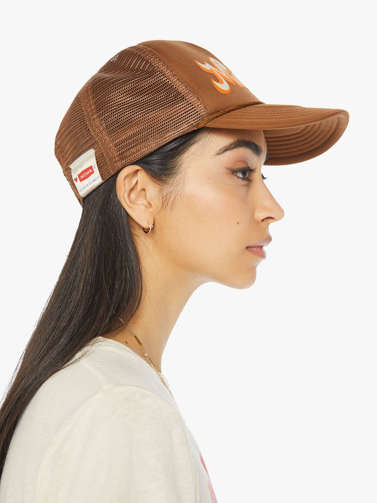 Side view of a woman in a brown trucker hat with MOTHER's name in orange and cream on the front.